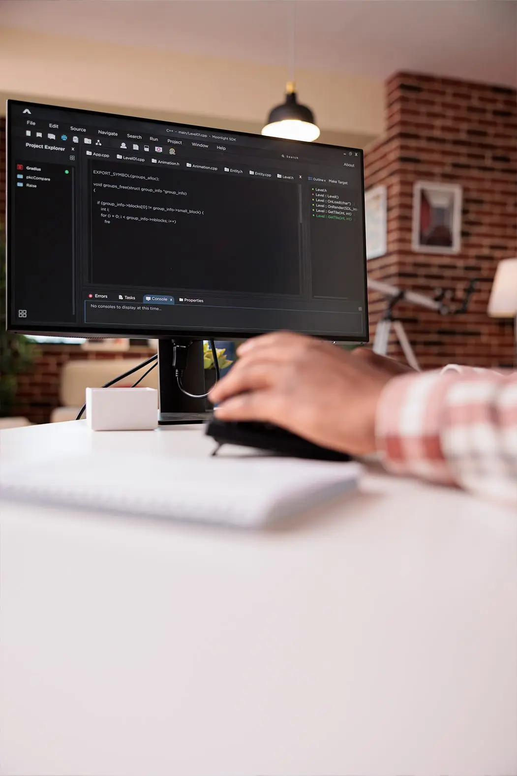 Hand mit Computermaus vor Bildschirm mit Codingzeilen